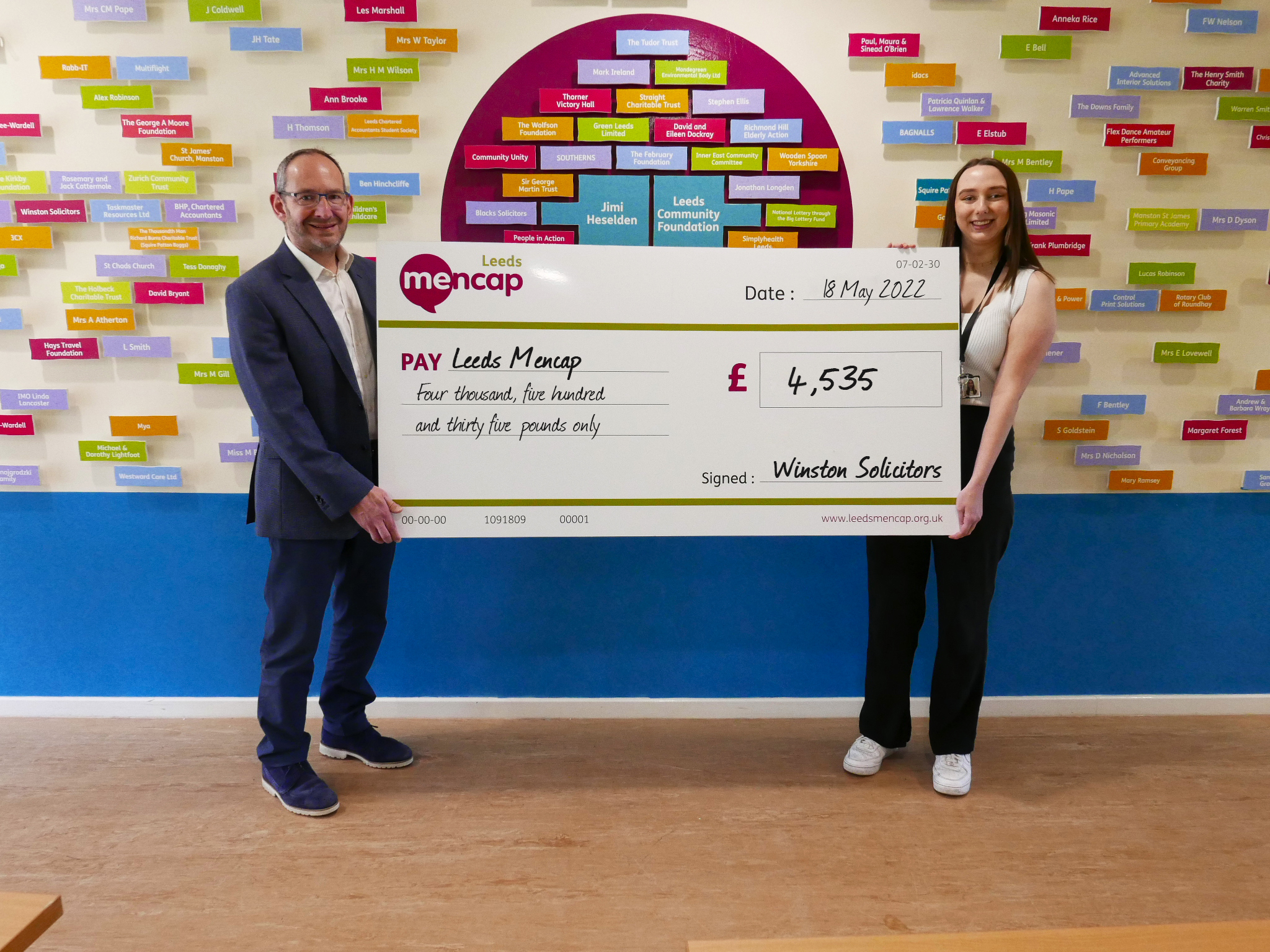 Two people holding a giant cheque for £4535 raised by Winston Solicitors for Leeds Mencap.