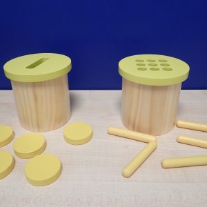 Two small wooden posting pots with yellow lids. One pot has a large straight opening for round disks, the other has small round holes for wooden tubes.